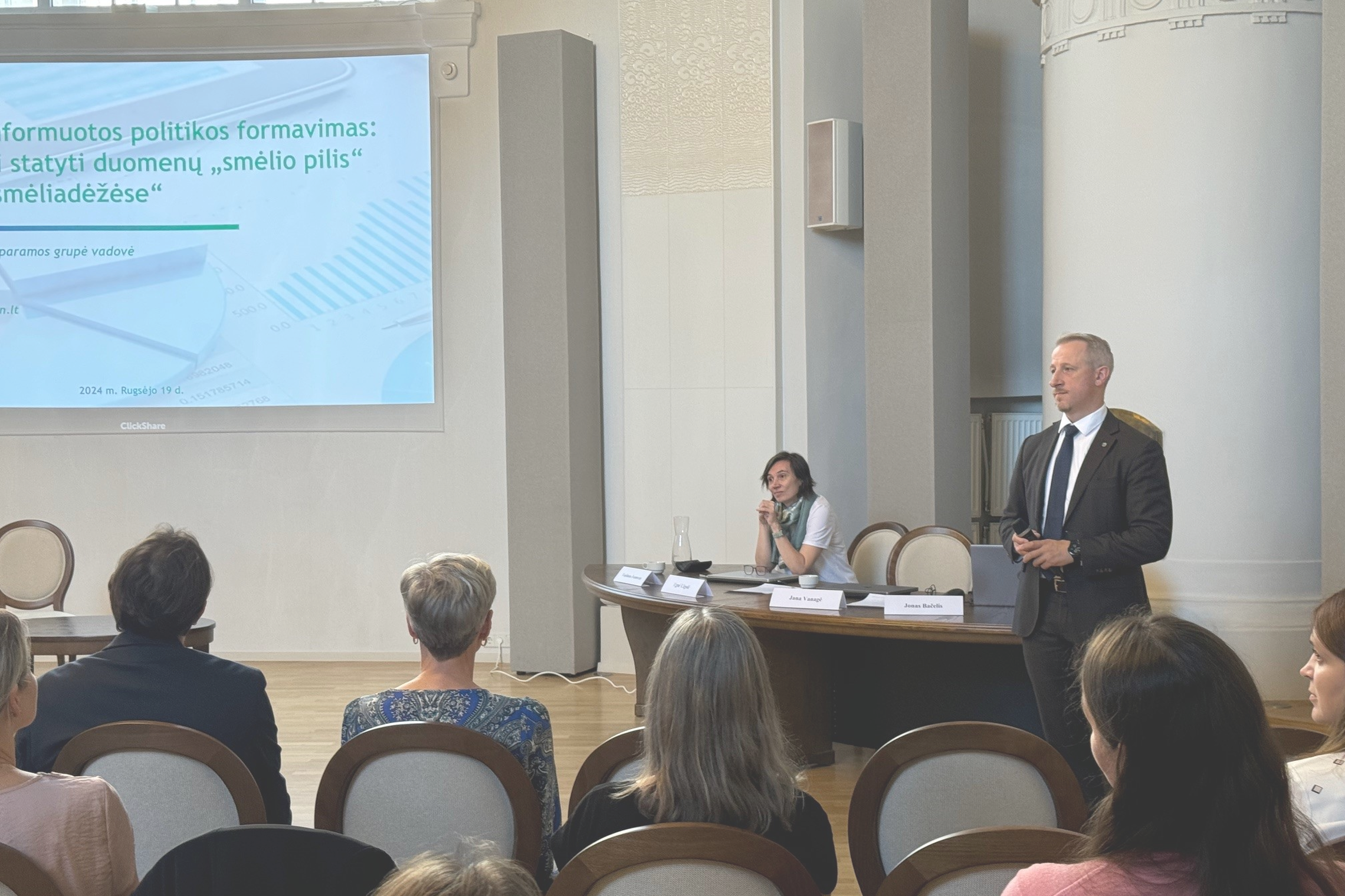 Salė, kurioje sėdi ir pristatymo klauso žmonės